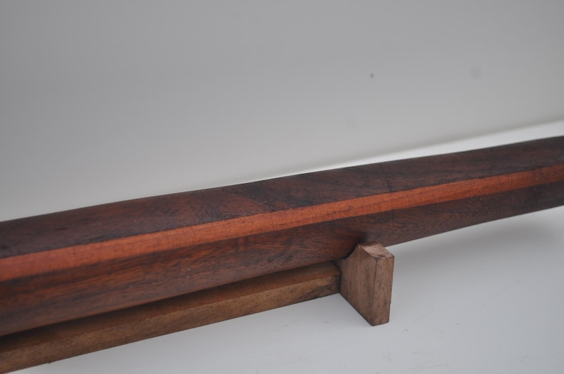 May include: A handcrafted wooden object with a dark brown exterior and a reddish-brown stripe. The object is supported by a smaller, lighter brown wooden base. The wood grain is visible, suggesting a natural finish.
