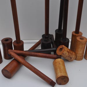 May include: A collection of wooden mallets and handles in various shades of brown and black. The mallets have cylindrical heads and long, slender handles. Some handles are detached, and some are assembled.