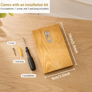 May include: A rectangular light brown wooden board with a metal keyhole hanger, accompanied by an installation kit containing one screwdriver, one screw, and one wall plug. The board measures 5.5 inches by 3.5 inches as indicated by text.
