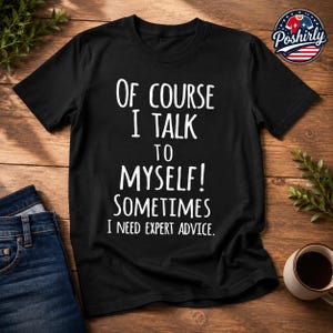 Puede incluir: Una camiseta negra de manga corta con el texto en blanco: Of course I talk to myself! Sometimes I need expert advice. La prenda cuenta con un cuello redondo y está confeccionada en tela negra lisa con letras blancas claras y centradas al frente.