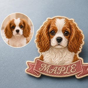 May include: A custom embroidered patch featuring a detailed portrait of a Cavalier King Charles Spaniel with brown and white fur. Below the dog's head is a pink ribbon banner with the name MAPLE stitched in white cursive lettering.