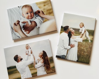 May include: Three rectangular photo canvases featuring family portraits. One shows a close-up of a baby being held, while the other two display a family of three in a field, with parents lifting their baby into the air against a natural outdoor backdrop.