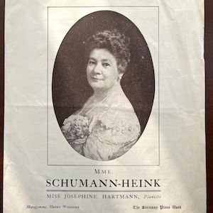 May include: A vintage black and white printed advertisement featuring a portrait of Mme. Schumann-Heink in an oval frame. Text includes MME. SCHUMANN-HEINK, MISS JOSEPHINE HARTMANN, Pianiste, Management, HENRY WOLFIOHN, and The Steinway Piano Used.