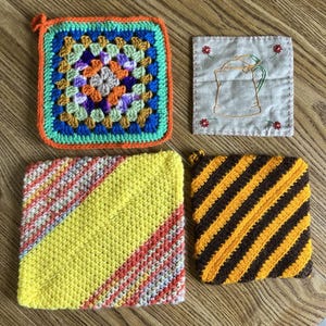May include: A collection of four square potholders: one multicolored granny square with an orange border, one beige fabric square with embroidered flowers and a teapot, one yellow and striped knit square, and one brown and yellow striped knit square.