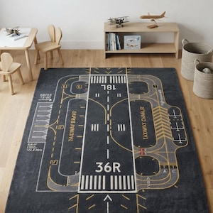 May include: A dark gray rectangular area rug featuring a detailed airport runway and taxiway design. The print includes white and yellow markings, runway numbers 18L and 36R, taxiway labels, gate indicators, and text reading Ramp Freq 122.8 MHz.