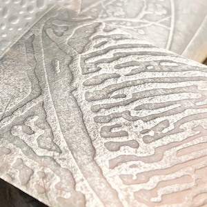 May include: Three silver metal plates with different embossed patterns. The plates are arranged in a stack, with the top plate showing a detailed, organic pattern.