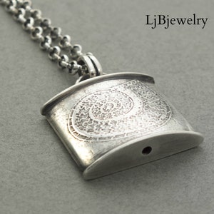 May include: Silver pendant necklace with a detailed spiral design. The pendant is rectangular with rounded edges and has a small hole at the bottom.