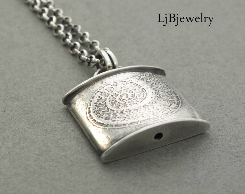 May include: Silver pendant necklace with a detailed spiral design. The pendant is rectangular with rounded edges and has a small hole at the bottom.