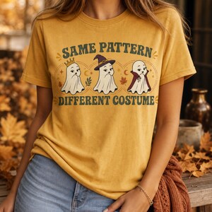 Puede incluir: Una camiseta de color amarillo mostaza con un gráfico de tres fantasmas blancos con diferentes atuendos, incluyendo una corona, un sombrero de bruja y una capa. El texto "SAME PATTERN" aparece sobre los fantasmas y "DIFFERENT COSTUME" debajo, con hojas de otoño.