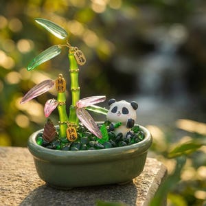 May include: A decorative ornament featuring a small panda figurine sitting in a green ceramic bowl filled with green glass pebbles. A bamboo plant with translucent green and pink leaves and small gold charms with Chinese characters is included.