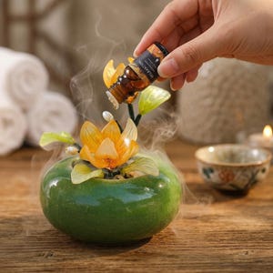 May include: A green ceramic bowl with a crackle glaze finish containing a decorative yellow flower sculpture. A small brown glass bottle labeled RELAXATION is held above, dispensing a clear liquid drop into the center of the flower.