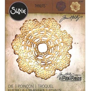 May include: A Sizzix Thinlits die set by Tim Holtz featuring a gold-colored, intricate, circular lace doily design. The packaging displays the Sizzix logo, the text Thinlits, 661497, and Tim Holtz Alterations. The die is centered on a tan background.