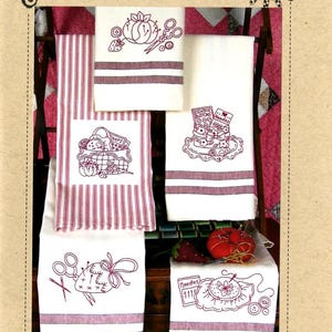 May include: A set of white kitchen towels featuring red embroidered sewing-themed designs including baskets, pincushions, scissors, and buttons. The text Bird Brain Designs and The RedWork Kitchen 478 is printed on the tan packaging card.