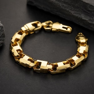 Könnte beinhalten: Ein goldfarbenes Armband bestehend aus einer Reihe dicker, ineinandergreifender rechteckiger Glieder mit einer polierten, reflektierenden Oberfläche. Das Schmuckstück verfügt über einen sicheren, integrierten Karabinerverschluss.