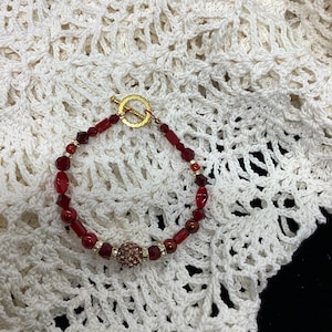 May include: A red and gold beaded bracelet with a large, sparkly, red and gold bead in the centre.