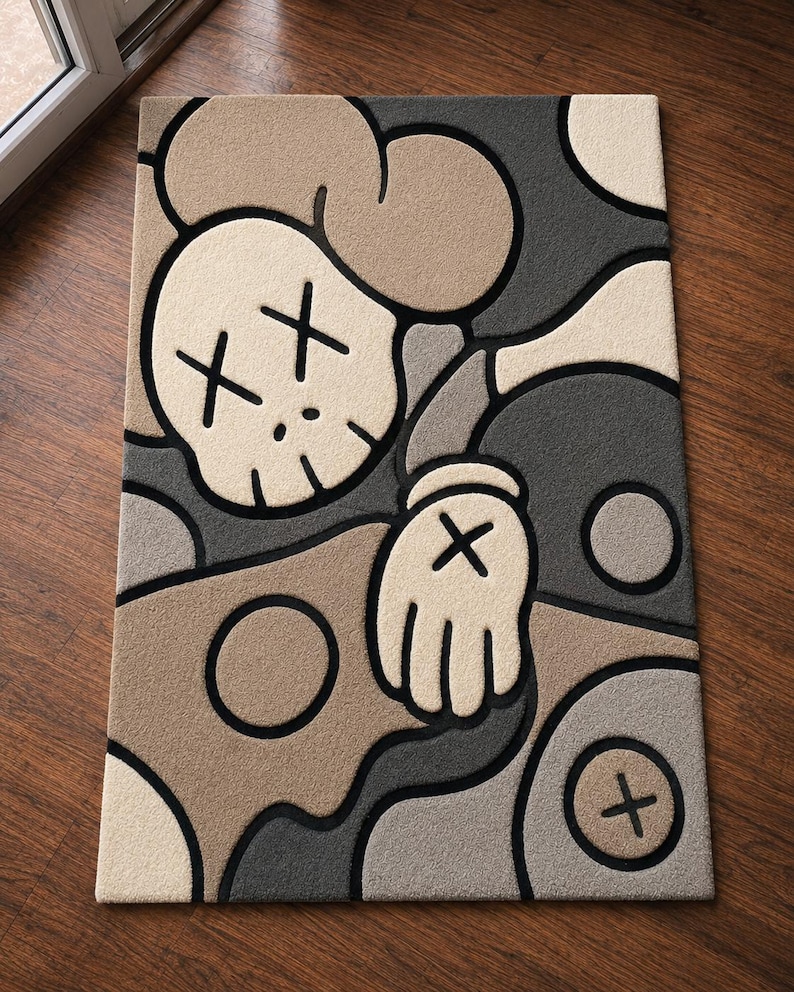 May include: A rectangular area rug featuring a stylized cartoon character design in shades of beige, tan, dark gray, and light gray. The graphic includes a skull-like head with X-shaped eyes, a gloved hand with an X, and circular motifs, all outlined in thick black lines.