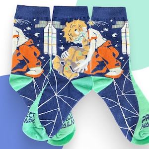 May include: A pair of dark blue crew socks featuring a graphic print of a character with light hair and glasses, space-themed elements including a satellite, stars, and the text Project Hail Mary in a geometric pattern on the light green heel and toe.