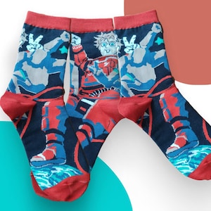 Könnte beinhalten: Ein Paar Socken mit dunkelblauem Hintergrund und einem Grafikdruck eines Astronauten im rot-blauen Anzug. Das Design zeigt eine Figur mit Friedenszeichen, eine stilisierte Erde am unteren Rand sowie rote Bündchen, Fersen und Zehen.