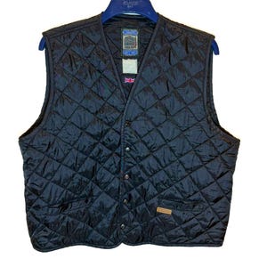 May include: A black quilted waistcoat featuring a diamond-patterned stitch, a V-neckline, and a front button closure. The garment includes two lower pockets, a small Union Jack flag detail, and a branded label at the inner neck and lower front.