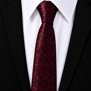 May include: A deep burgundy necktie featuring a repeating black geometric pattern. The tie is knotted and positioned against a crisp white dress shirt, which is layered underneath a structured black blazer with sharp lapels and visible stitching.