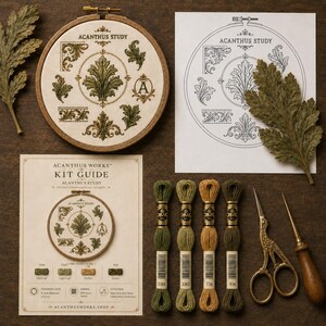 May include: An embroidery kit titled Acanthus Study featuring a wooden hoop with stitched acanthus leaf motifs, a printed pattern guide, four skeins of embroidery floss in green and gold tones, gold-toned stork scissors, and a wooden awl.
