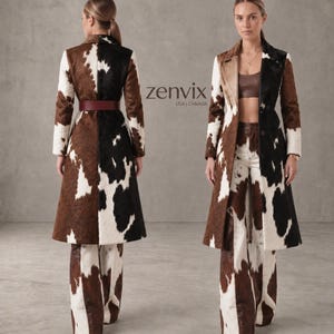 May include: A long coat and matching wide-leg trousers featuring a cow-print pattern in brown, black, and white. The coat has a collar, long sleeves, and a dark red belt. The text "zenvix USA | CANADA" is visible in the center of the image.