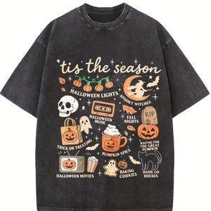 May include: A charcoal grey short-sleeve t-shirt featuring a graphic print with the text 'tis the season' and various Halloween-themed illustrations including pumpkins, a skull, a witch, a ghost, a cassette tape, and a mug of pumpkin spice.