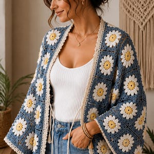 Può includere: Un cardigan all'uncinetto con un motivo a quadrati blu e disegni di margherite bianche e gialle. Il capo presenta un'apertura frontale con un bordo color crema, maniche lunghe e ampie e due nappe color crema pendenti in vita.