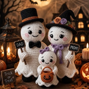 May include: Three crocheted ghost figures representing a family. The larger ghosts wear a black top hat and a black witch hat with flowers. The smaller ghost holds an orange pumpkin bucket. They hold signs labelled DAD and MOM.