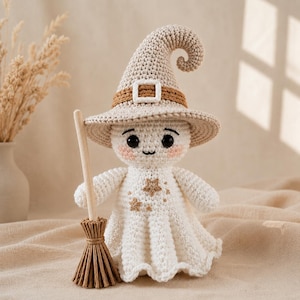 May include: A crocheted ghost doll wearing a beige pointed hat with a brown band and white buckle. The ghost has black eyes, pink cheeks, and a small mouth. It features embroidered gold stars on its chest and holds a small wooden broom.