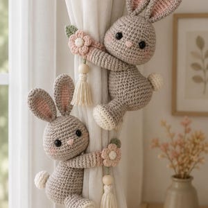 Peut inclure: Deux embrasses de rideaux en forme de lapins gris crochetés avec des oreilles intérieures roses, des yeux noirs et des queues blanches. Chaque lapin tient une petite fleur rose avec une feuille verte et une perle en bois crème avec un pompon.