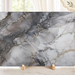 May include: A rectangular cutting board featuring a marbled pattern in shades of charcoal grey, white, and black with subtle gold veining throughout. The board is supported by a small wooden stand, displaying a smooth, polished surface texture.