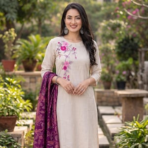 May include: A beige three-piece outfit consisting of a long-sleeved straight-cut tunic with pink and dark pink floral embroidery, matching straight-leg trousers with a pink hem detail, and a deep purple shawl featuring a detailed floral pattern.