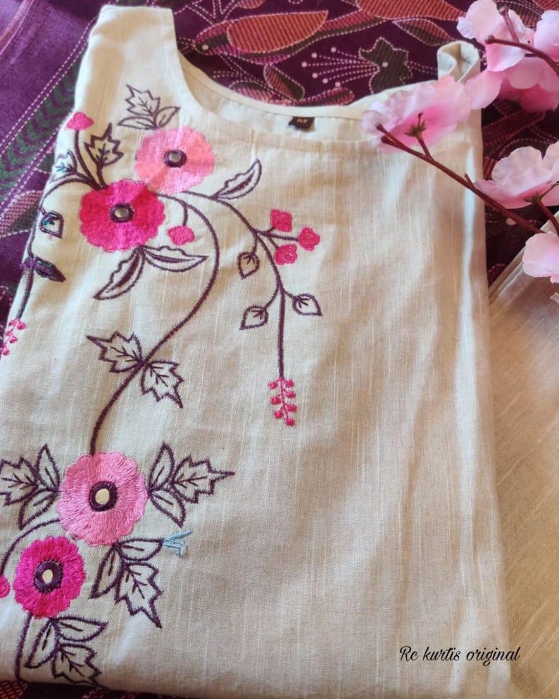 May include: A beige sleeveless tunic featuring embroidered pink flowers with dark purple stems and leaves. The garment has a round neckline and includes the text "Rc kurtis original" printed in the bottom right corner of the fabric.