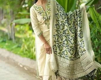 May include: A cream-coloured three-piece outfit consisting of a long-sleeved tunic with green floral embroidery around the neckline, matching straight-leg trousers with embroidered cuffs, and a large shawl featuring a detailed green leaf print.