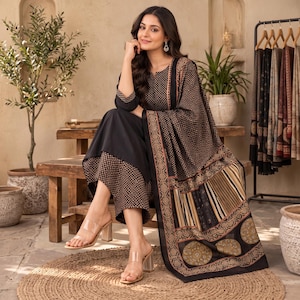 May include: A black three-piece outfit consisting of a long-sleeved tunic with a small geometric pattern, matching wide-leg trousers, and a large shawl featuring a mix of geometric, striped, and circular motifs in shades of black, brown, and tan.