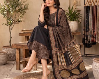 May include: A black three-piece outfit consisting of a long-sleeved tunic with a small geometric pattern, matching wide-leg trousers, and a large shawl featuring a mix of geometric, striped, and circular motifs in shades of black, brown, and tan.