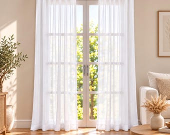 May include: A pair of floor-length white sheer curtains hanging from a silver metal rod over a glass-paned double door. The curtains feature a pleated top header and a lightweight, semi-transparent fabric that allows natural light to filter through.