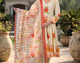 May include: A cream-colored long-sleeved tunic with a V-neckline, featuring orange and yellow floral prints, paired with matching trousers and a sheer, rectangular scarf adorned with a vibrant floral and checkered pattern in shades of red and orange.