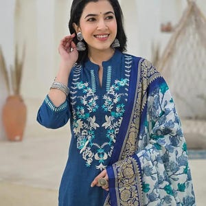 May include: A deep blue kurta featuring a mandarin collar and intricate white and teal floral embroidery along the neckline. The ensemble includes a matching dupatta with a white and teal floral print and a wide, ornate gold-toned border.