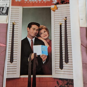 May include: A vintage advertisement for Wembley neckwear featuring a man in a dark suit and a woman in a red top standing in a window frame. Several patterned neckties hang from white shutters. The text reads Wembley, Gibraltar Foulards, and Happy Birthday.