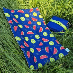 May include: A rectangular blue fabric mat featuring a repeating pattern of watermelon slices and kiwi fruit segments, with the text "summer time" printed in small white letters. A folded blue pouch with a lime green strap is positioned nearby.