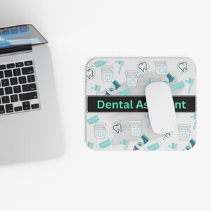 May include: A rectangular mouse pad featuring a repeating pattern of dental icons including teeth, toothbrushes, toothpaste, and floss containers. A central black horizontal bar displays the text Dental Assistant in light green letters.