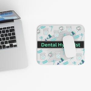 May include: A rectangular mouse pad featuring a repeating pattern of dental icons including teeth, toothbrushes, toothpaste, and floss containers. A central black horizontal bar displays the text Dental Hygienist in light green letters.