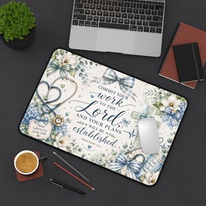 May include: A rectangular desk mat featuring a floral design with blue and white ribbons, a stethoscope, and the text: COMMIT YOUR WORK TO THE LORD AND YOUR PLANS WILL BE ESTABLISHED. PROVERBS 16:3. A small tag reads: Nurse Called to Care Led by Faith.