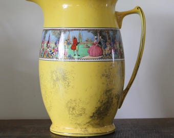 May include: A bright yellow ceramic pitcher featuring a central horizontal band decorated with a colorful garden scene depicting figures in period clothing. The pitcher has a curved handle, a pouring spout, and a weathered, mottled finish.