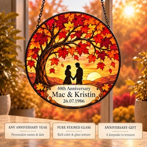 Op de afbeelding: Een ronde glas-in-lood zonnevanger met een boom met levendige rode en oranje herfstbladeren. Onder de boom staat het silhouet van twee personen tegen een zonsondergang. De tekst luidt 40th Anniversary, Mac & Kristin, 26.07.1986.