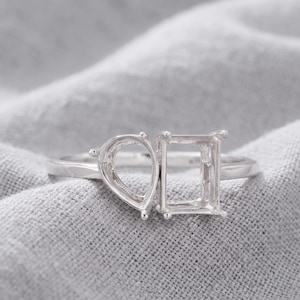 May include: A silver-toned metal ring featuring two empty prong settings. One setting is shaped like a pear, and the other is rectangular. The ring band is smooth and polished, designed to hold two stones side-by-side in this open setting style.