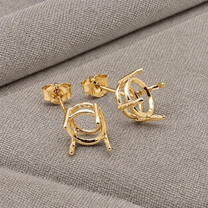 Könnte beinhalten: Ein Paar goldfarbene Ohrstecker-Fassungen mit einem kreisförmigen Korbdesign und vier Krappen zur Aufnahme eines Edelsteins. Jeder Ohrstecker verfügt über einen Stift und einen passenden Schmetterlingsverschluss mit glänzender Oberfläche.