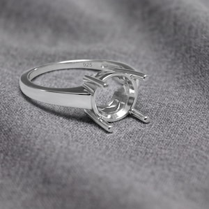 May include: A polished silver ring setting featuring a four-prong head designed to hold a round gemstone. The inner band of the ring is clearly stamped with the number 925, indicating sterling silver construction for this jewelry component.